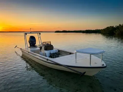 A 14-foot flats skiff with a forward casting deck and push pole staked off on clear shallow saltwater at golden hour.